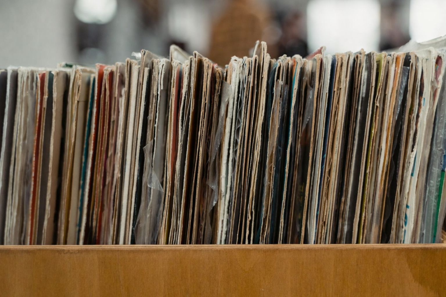 Närbild på en rad med gamla, dammiga vinylskivor i ett brunt träfack.
